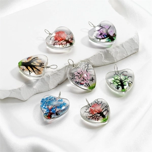 Détail de pendentifs en verre en forme de cœur avec arbre de vie et fleurs séchées