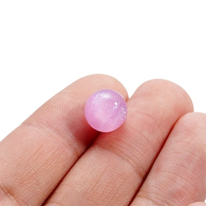 Primo piano di una perla in resina rosa con glitter tenuta tra le dita