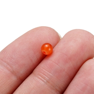 Vue macro d'une perle en verre translucide rouge-orangé sur un doigt pour bijoux DIY