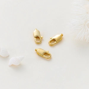 Detailansicht von drei vergoldeten Karabinerverschlüssen für DIY-Schmuck auf Naturhintergrund
