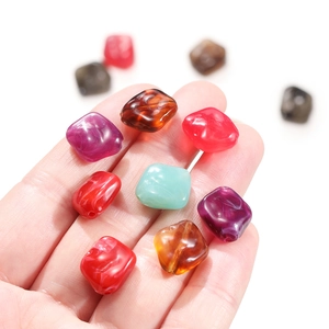Hand holding colorful irregular acrylic beads for DIY jewelry with marble texture effects