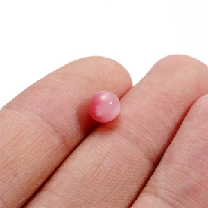 Macro view of a 6-8mm pink cat-eye resin bead held by fingers for size reference