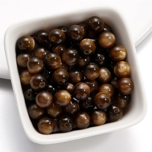 Macro view of 6/8mm resin cat eye beads with golden sheen in a white ceramic bowl