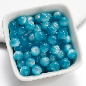 Macro shot of 8mm lake blue cat eye resin beads with center hole in a white ceramic bowl