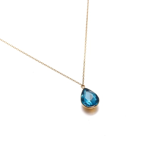 Detalle de un collar de cadena fina dorada con un colgante de cristal azul en forma de gota
