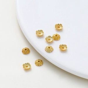 Detailed view of 18k gold-plated floral bead caps on a white ceramic plate for DIY jewelry