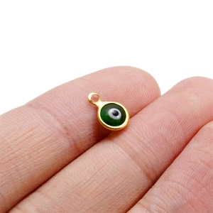 Macro shot of gold-plated stainless steel green evil eye connector charm on a finger