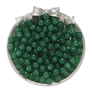 Macro detail of dark green apple-shaped glass beads for jewelry making in silver dish