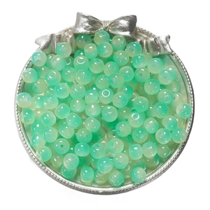Close-up of translucent light green glass apple beads on a silver tray for DIY jewelry