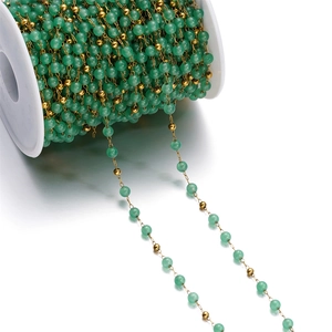 Detail view of green glass beads and gold chain links on a white plastic spool