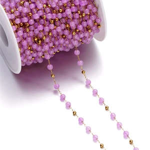Macro detail of purple cat eye glass beads and gold chain on a DIY craft jewelry spool