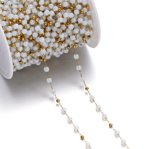 Macro detail of cat eye glass beads and gold chain on a white spool for DIY jewelry