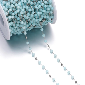 Detailed close-up of sky blue cat eye beads and silver metal chain on a white spool