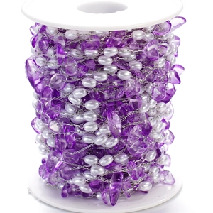 Macro detail of purple gemstone and pearl beaded stainless steel chain on a white spool