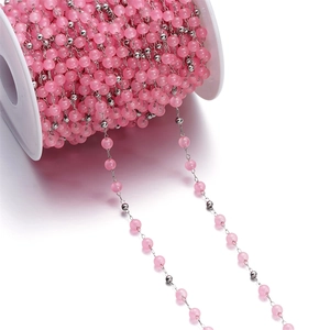 Detail of pink cat-eye glass beads and silver stainless steel chain on white spool