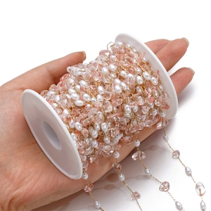 Detailed macro view of pink glass stone and white pearl beads on a gold metal DIY chain