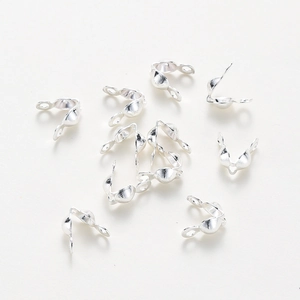 Macro view of silver-plated bead tips for jewelry making on cream background