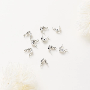 Silver bead tips and calottes connectors for jewelry making displayed with white flowers