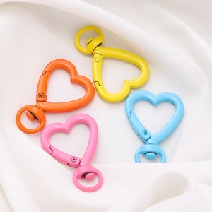 Dettaglio di moschettoni a cuore da 26mm in colori pastello opachi su raso bianco