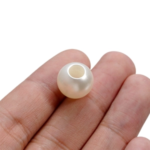 Vue macro d'une perle ABS blanc crème entre les doigts montrant la taille réelle