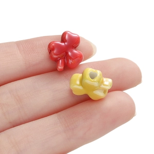 DIY ceramic clover beads in red and yellow for necklace making held by fingers