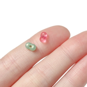 Macro view of 4mm peanut-shaped acrylic beads on a finger for DIY jewelry making