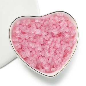 Macro detail of 4mm matte pink peanut-shaped acrylic beads in a white ceramic heart dish