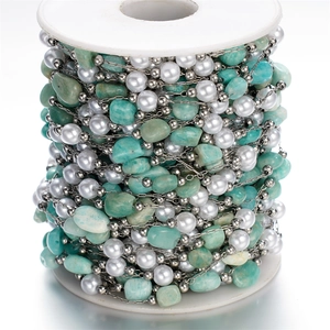 Detail of DIY stainless steel jewelry chain with green stones and pearls on white spool