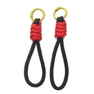 Détail d'une dragonne en paracorde tressée rouge et noire avec mousqueton jaune