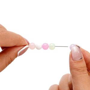 Close-up of DIY beading needle threading colorful translucent beads for jewelry making
