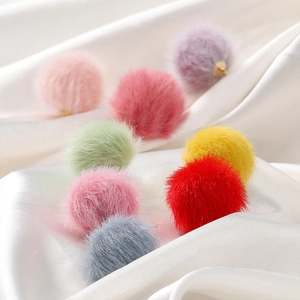 Close-up of colorful 17mm faux mink fur pompoms with gold loops on white silk fabric