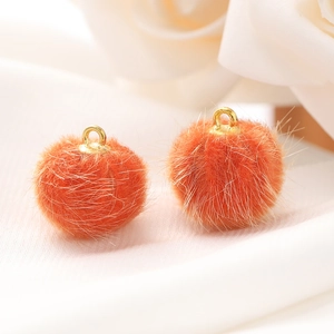 Detail van twee oranje 15 mm imitatiebont pompons met gouden lussen voor DIY-sieraden
