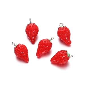 Detail view of five red resin strawberry pendants with green leaves and metal rings for DIY