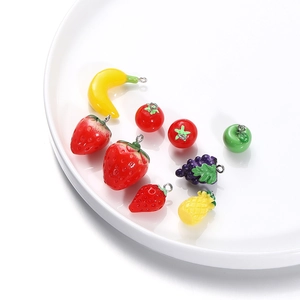 Assorted resin fruit charms with metal rings for DIY jewelry making on white ceramic plate