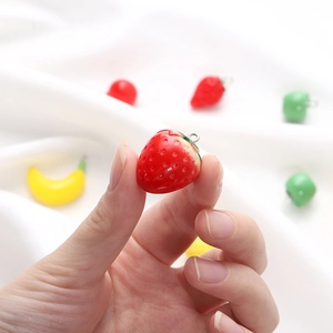 Close-up of a resin strawberry pendant charm for DIY jewelry being held by hand