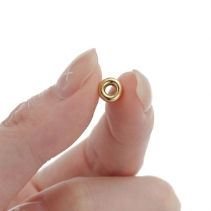Macro shot of a tiny gold polished 925 silver flat spacer bead held between fingers