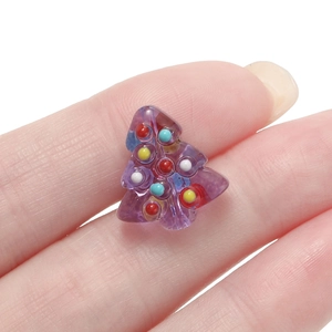 Macro shot of a tiny purple resin Christmas tree bead with colorful dots on a fingertip