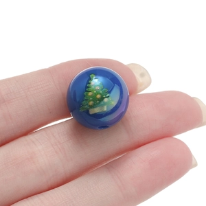 Detail of blue acrylic Christmas tree bead being held for DIY jewelry craft sizing