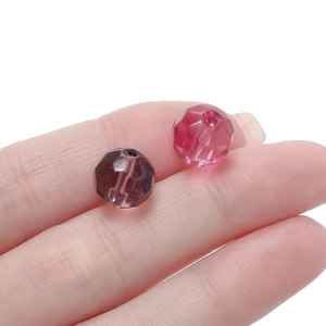 Detailed macro view of 10mm faceted gradient glass beads held on fingertips for DIY jewelry