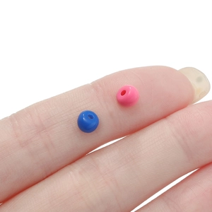 Dettaglio di piccole perline acriliche blu e rosa su un dito per la creazione di gioielli