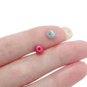 Dettaglio di perline in acrilico rosa e verde acqua sulle dita per creazione di gioielli