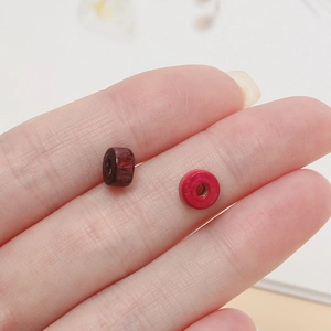 Macro shot of colorful cylindrical wooden beads for DIY jewelry making on a fingertip