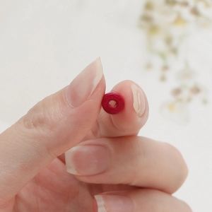 Close-up of a small red wooden macaron bead held between fingers for DIY jewelry
