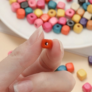 Close-up of a hand holding a colorful square wooden bead for DIY jewelry and crafts
