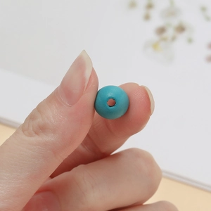 Vue macro d'une perle en bois bleu cyan mat avec trou central pour la création de bijoux