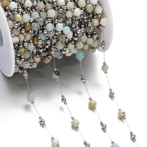 Macro detail of natural faceted stone chain with stainless steel beads on a white spool