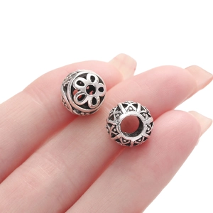 Detailed macro of hollow silver beads with geometric engraving held between fingers