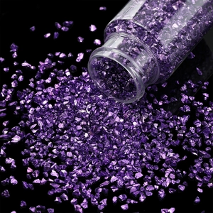 Nahaufnahme von violetten Glassteinen, die aus einer Flasche auf schwarzen Spiegel fallen
