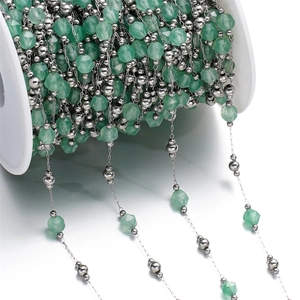 Detailed close-up of green faceted stone beads and silver metal chain on a white spool