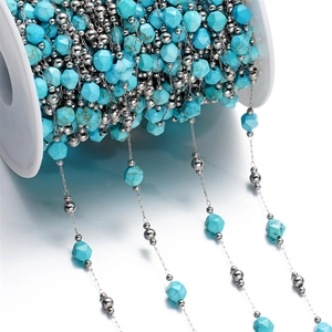 Close-up of turquoise faceted stone beads and silver metal beads on a white spool